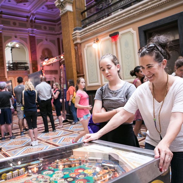 A photograph of a woman playing pinball inside the Smithsonian American Art Museum during SAAM Arcade.