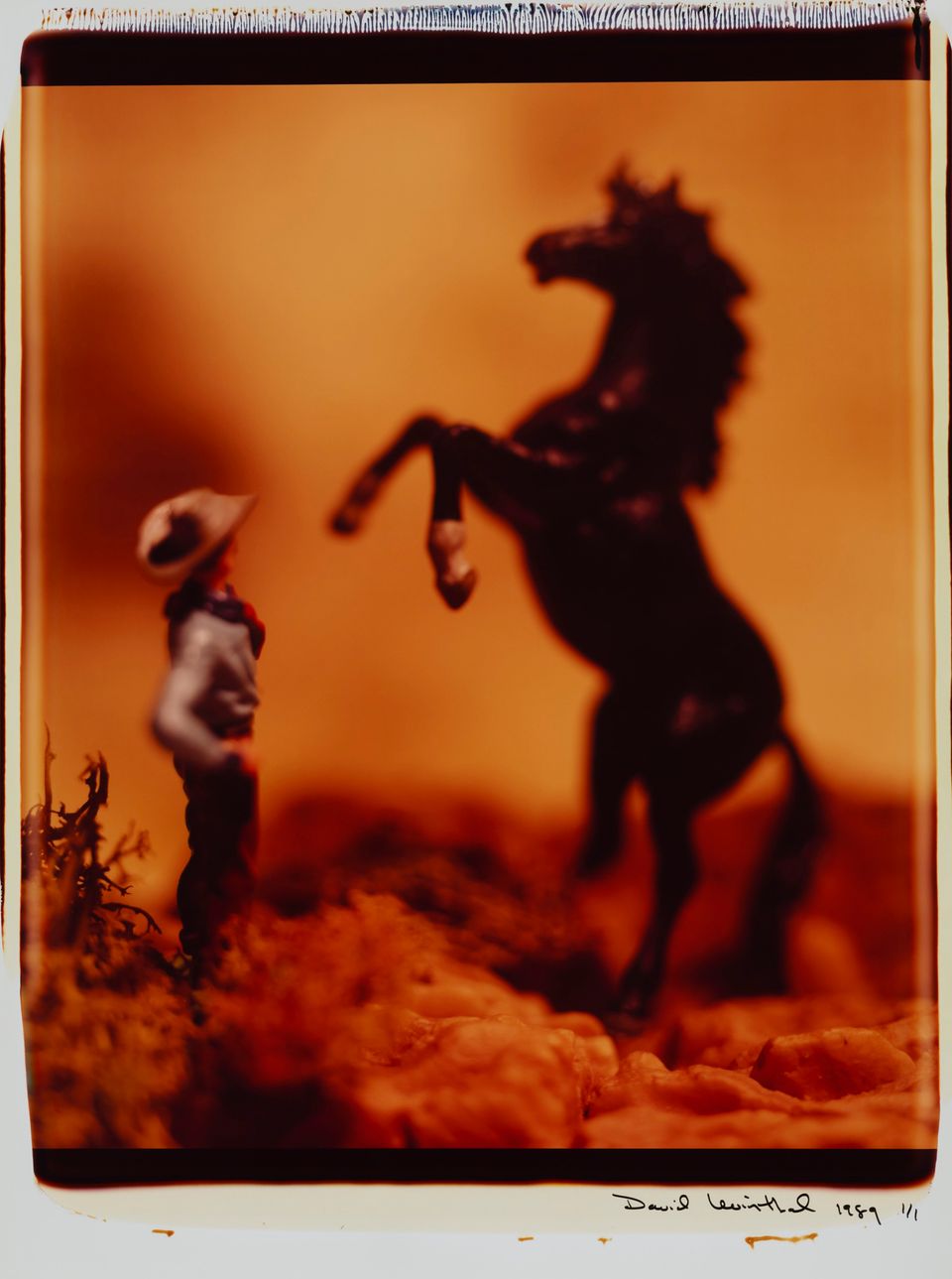 A photograph of a toy horse on it's back legs and a man standing in front of it.
