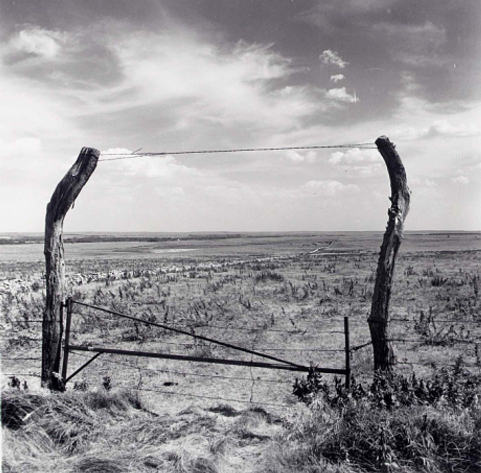 This picture shows a fence in an open, barren field in black and white