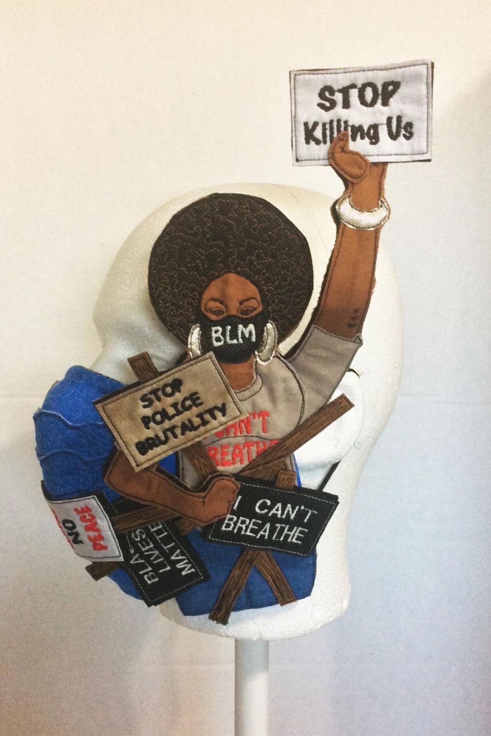 An applique sculpture of a woman in a mask holding protest signs.