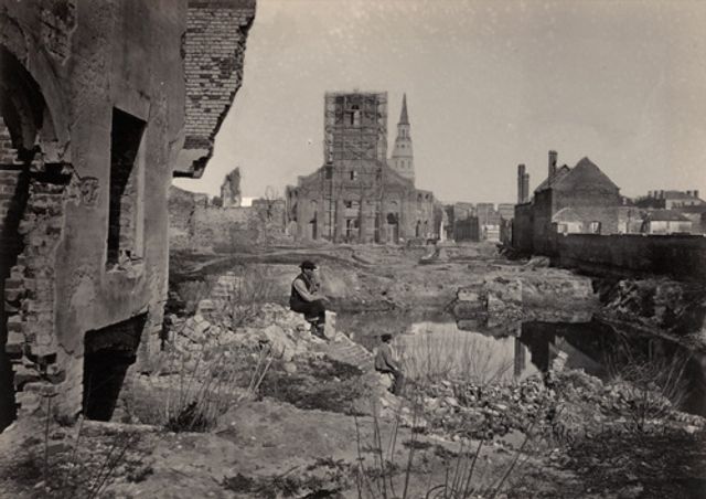 Barnard's vintage albumen print of a town with a man sitting on rocks in the middle ground and the surrounding town in the background.