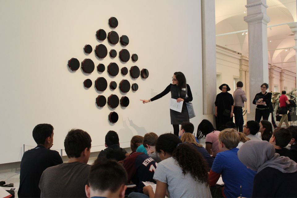 An educator discusses an artwork in front of a large group of students