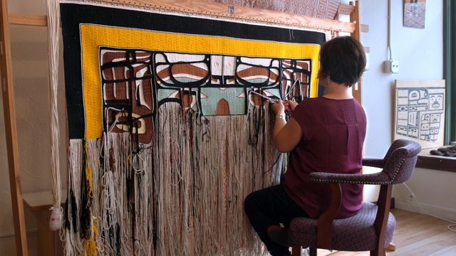 A woman sitting at a large loom, weaving a blanket