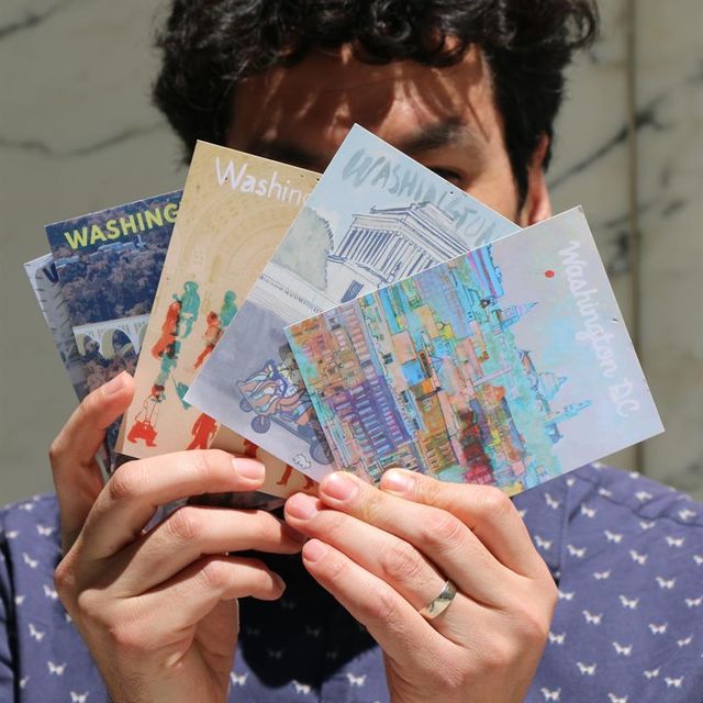 The artist holding some of his illustrated DC postcards